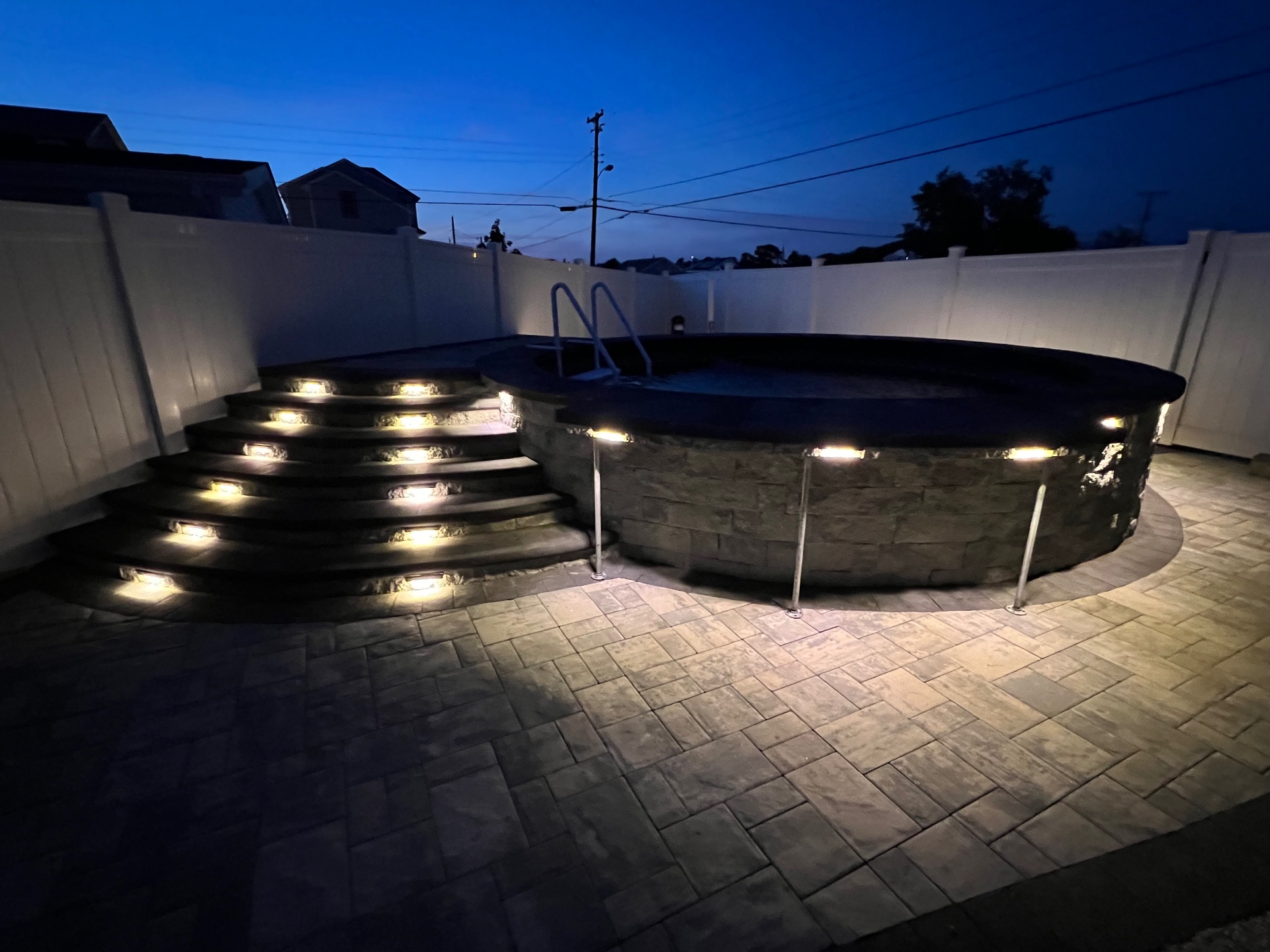 Lit pool patio with paver surround at dusk